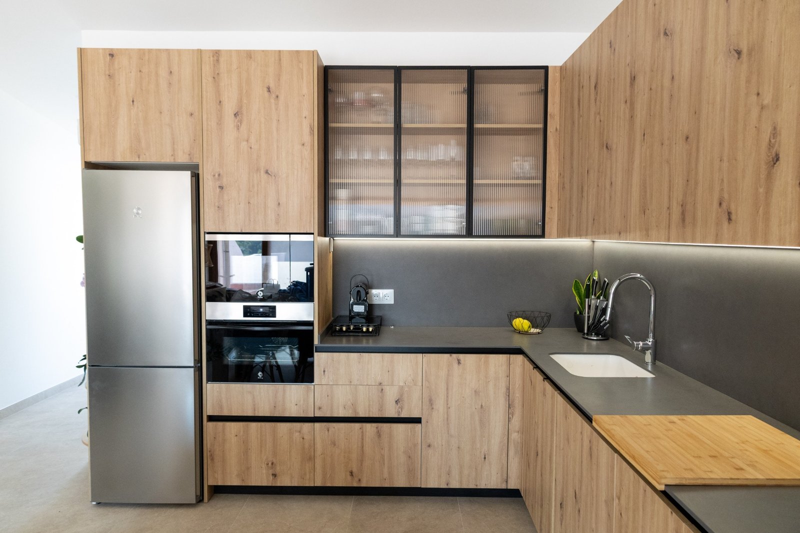 Cocina NF Cuines con frentes de madera, encimera gris y vitrina de cristal acanalado